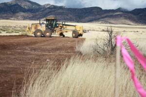 A Hummel Construction employee grades the road which will run alongside 26 turbines at the Red Horse 2 Wind Farm. The pink-ribboned stakes in a row at right designate turbine placement.
