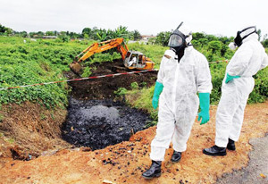 Abidjan, IVORY COAST:  Two civil protection workers pass by a bulldozer clearing a site polluted with toxic waste at the Akouedo district in Abidjan 19 September 2006. In mid-August the Probo Koala ship unloaded in Abidjan more than 500 tonnes of a highly toxic mixture of oil residue and caustic soda used to rinse out the ship's tanks. The poisons are known to cause nausea, rashes, fainting, diarrhoea and headaches. Besides the seven deaths, 24 people are still hospitalized and more than 37,000 have sought medical treatment.    AFP PHOTO/Issouf SANOGO  (Photo credit should read ISSOUF SANOGO/AFP/Getty Images)