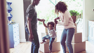 A photo of playful parents holding daughter's hands in new house. Happy and playful family are with cardboard boxes. They are in casuals.